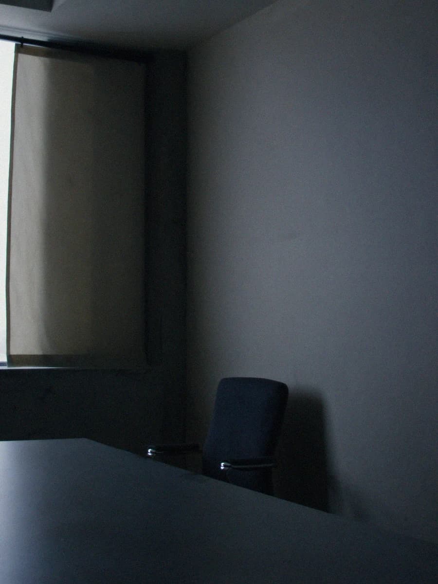 Pusty fotel przy stole konferencyjnym, zasłonięte okno, chłodne światło
